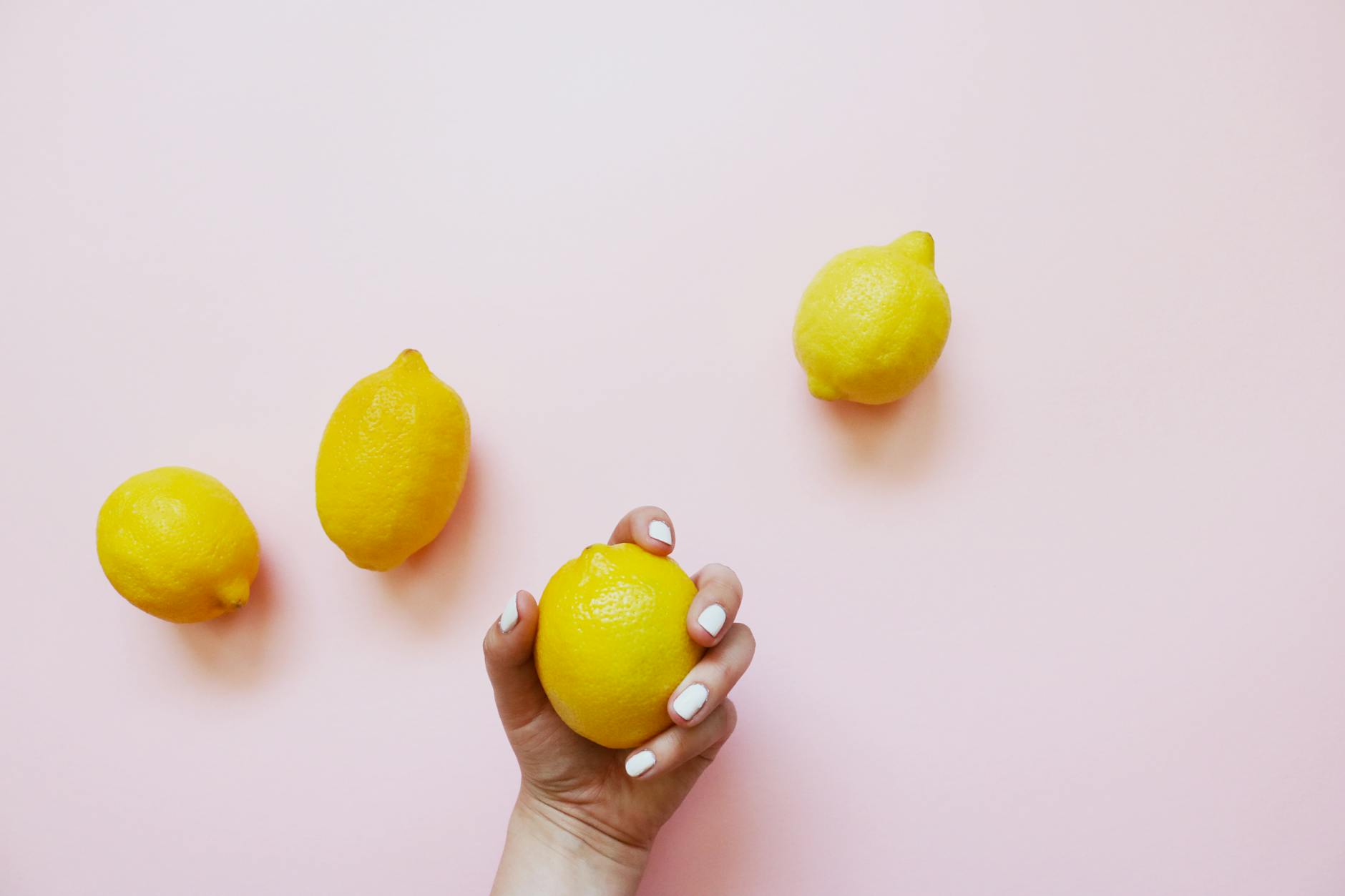 A hand holding a lemon against a soft pink background, symbolizing self-care and solo pleasure