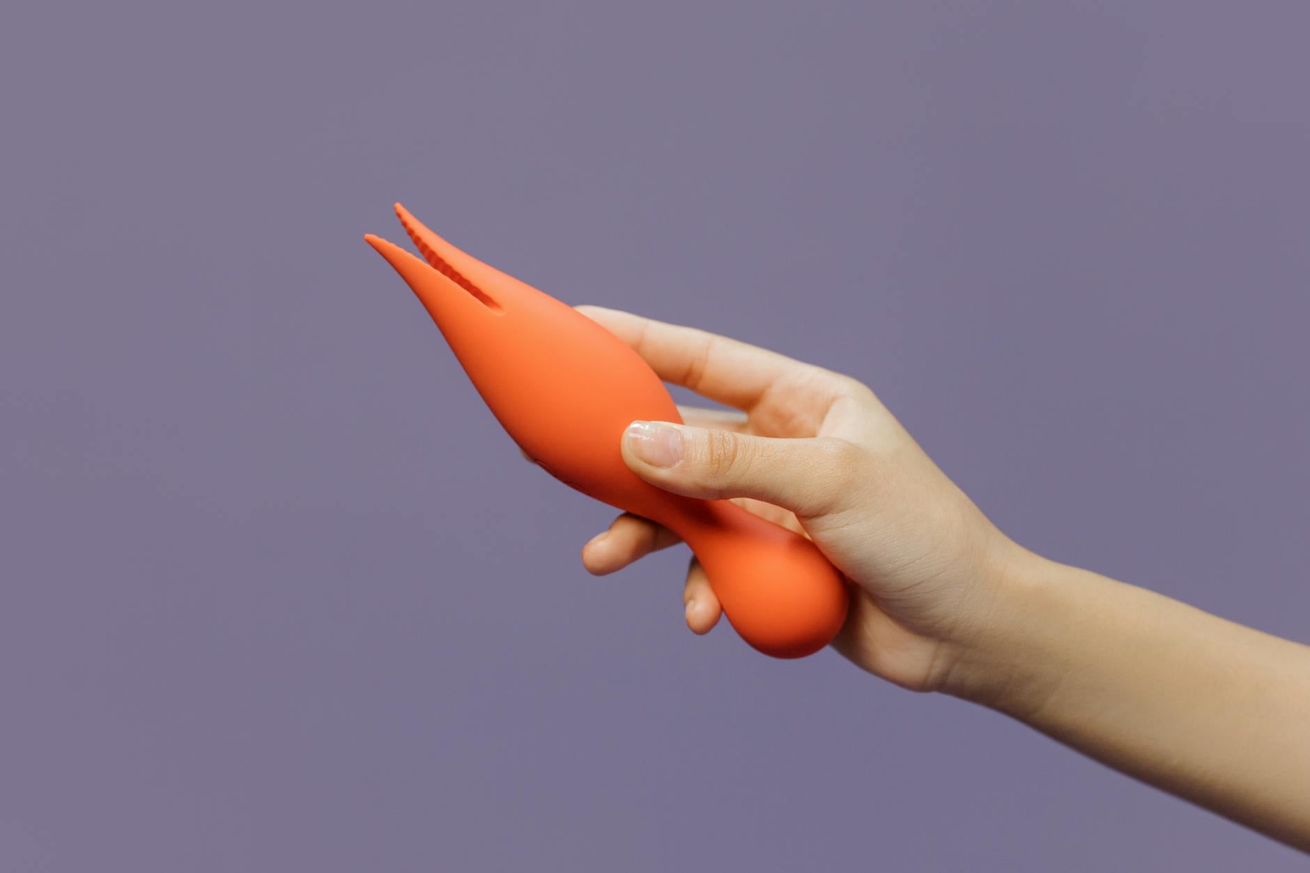 A hand holding a lemon-colored clitoral vibrator against a minimalist backdrop.