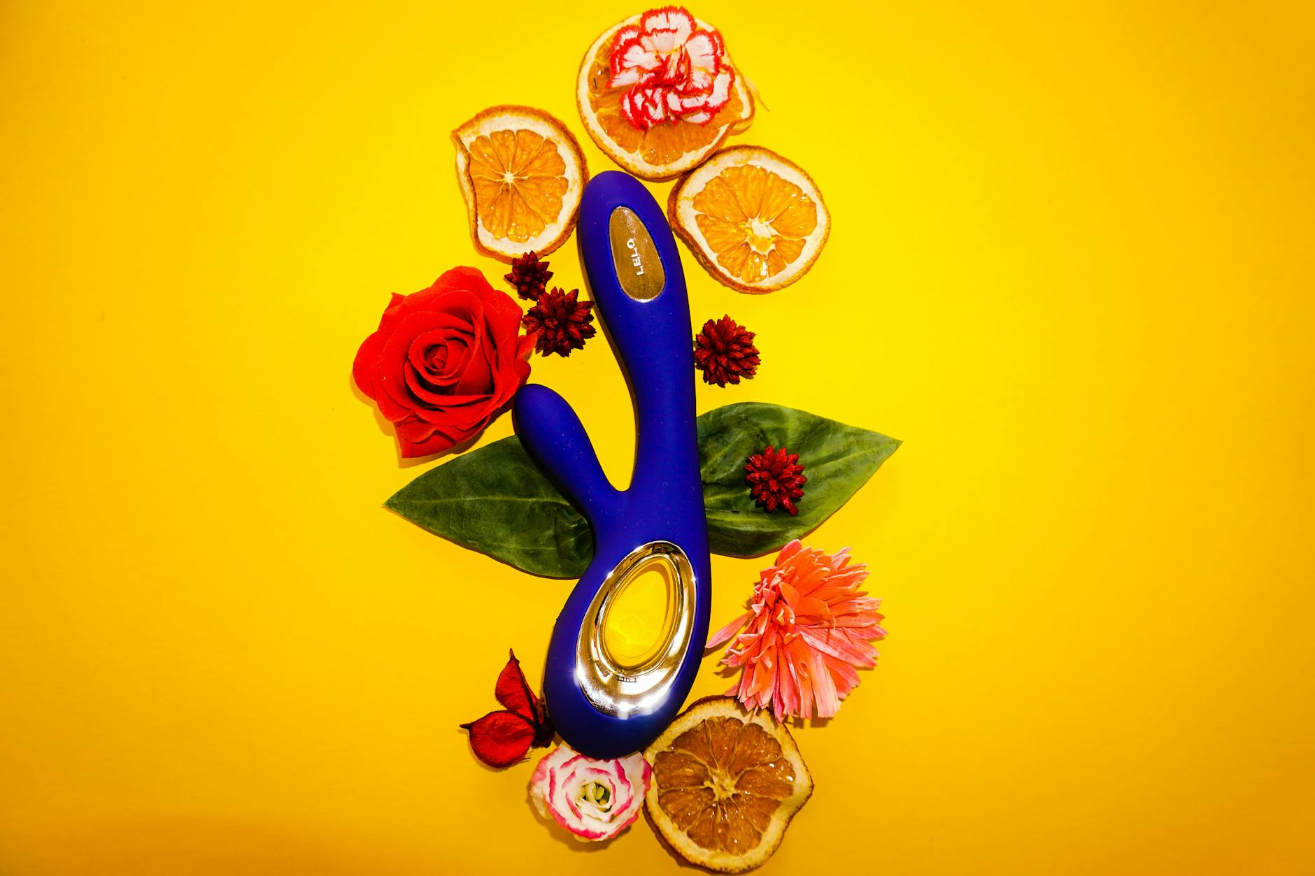 A blue lemon vibrator surrounded by flowers and citrus slices on a bright yellow background.