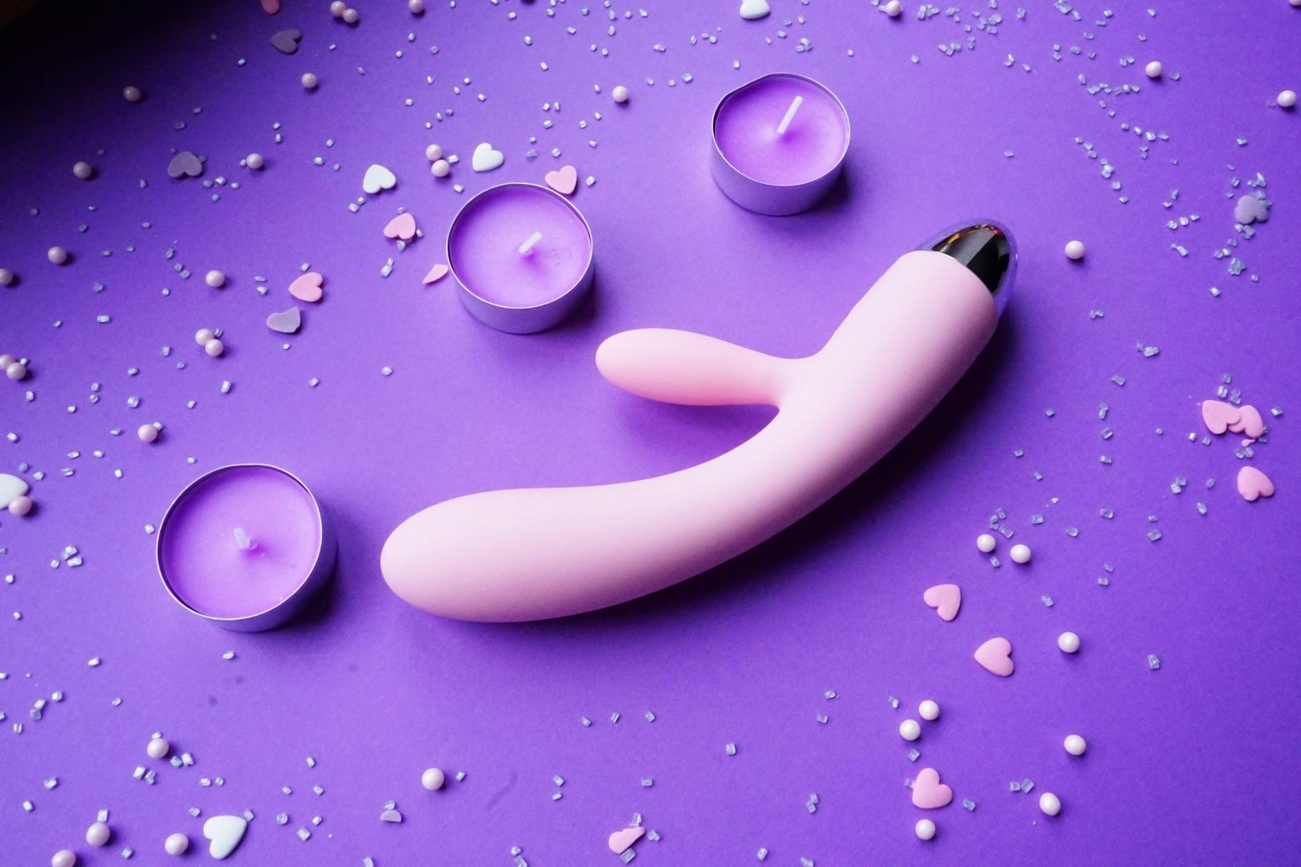 Pink lemon vibrator on purple background with heart confetti and candles for romantic moment